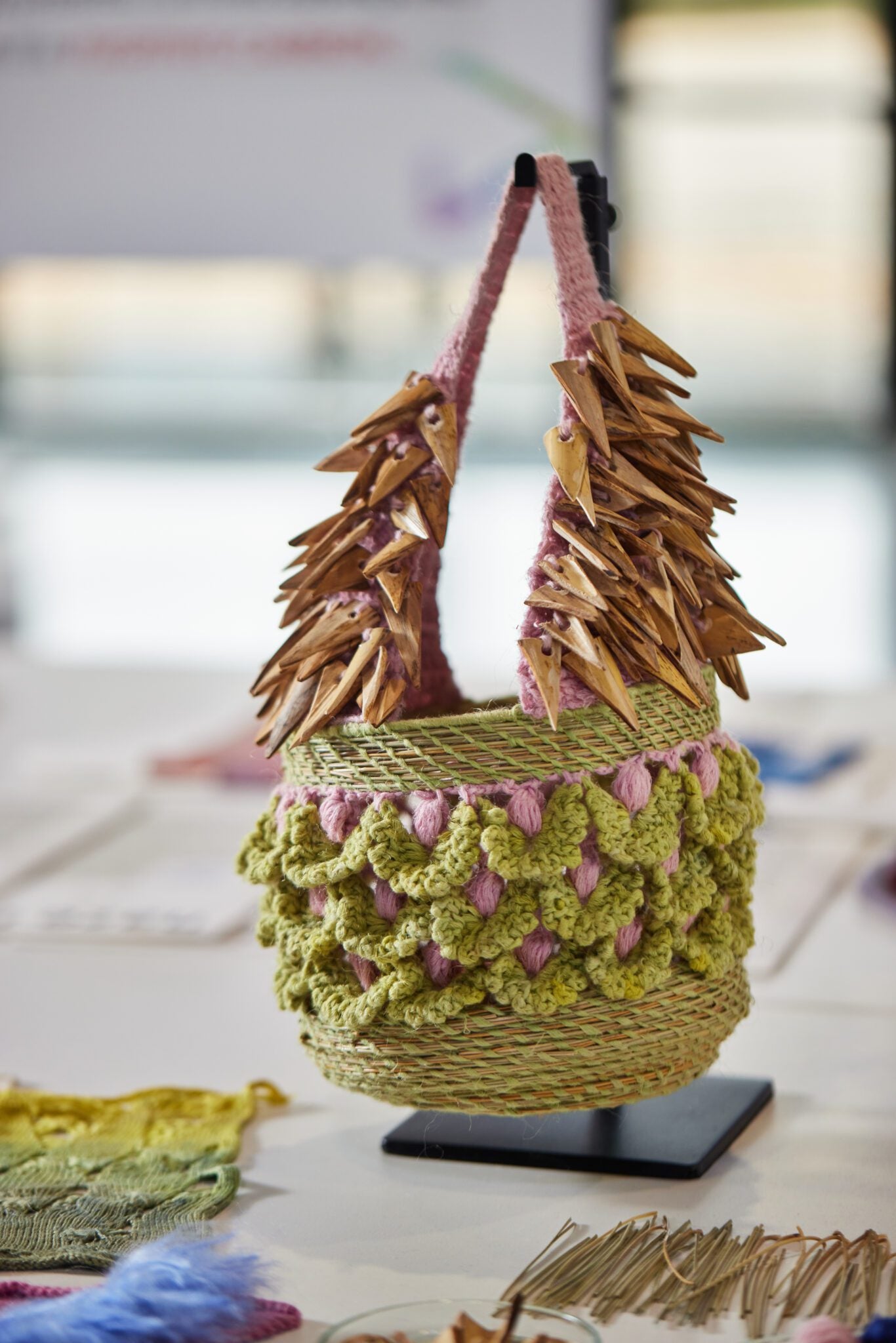 Close up of REGENERATIVE FOLKLORE bag showcased at The Future Fabrc Expo. Green and pink crochet bag with woven dry branch details, adorned with hand cut Almería canes. 